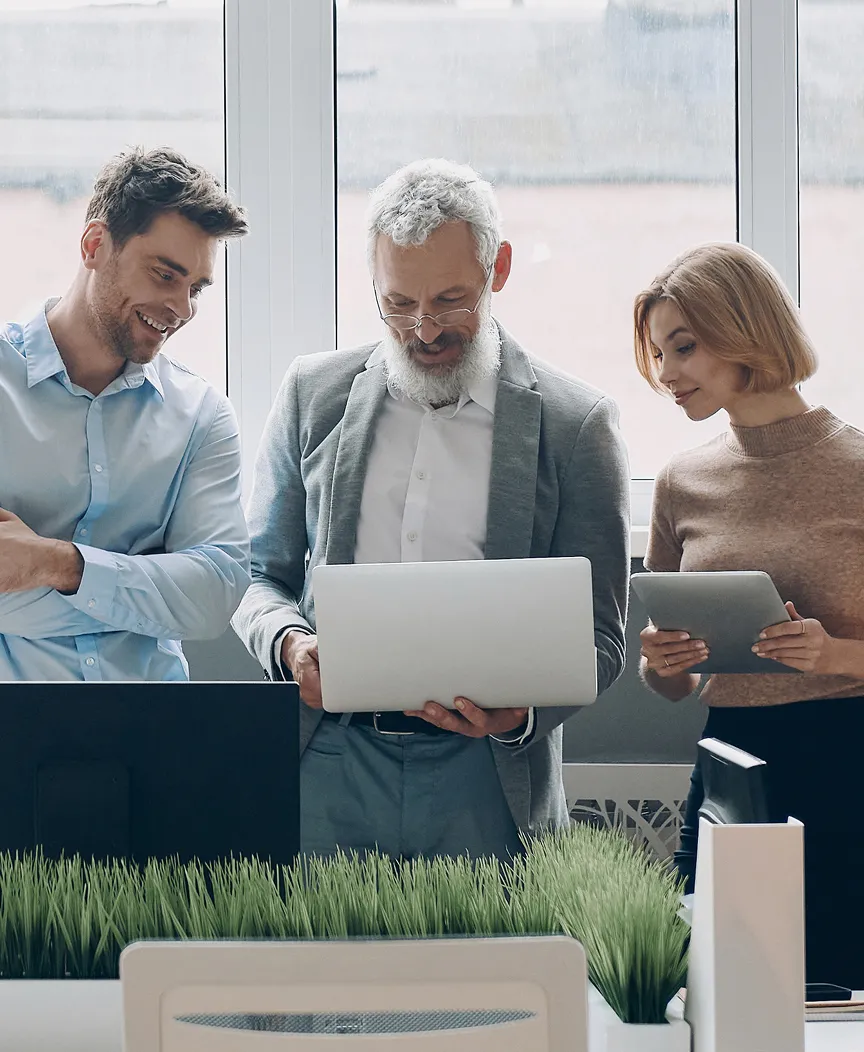 Three people standing up in an office looking at a laptop