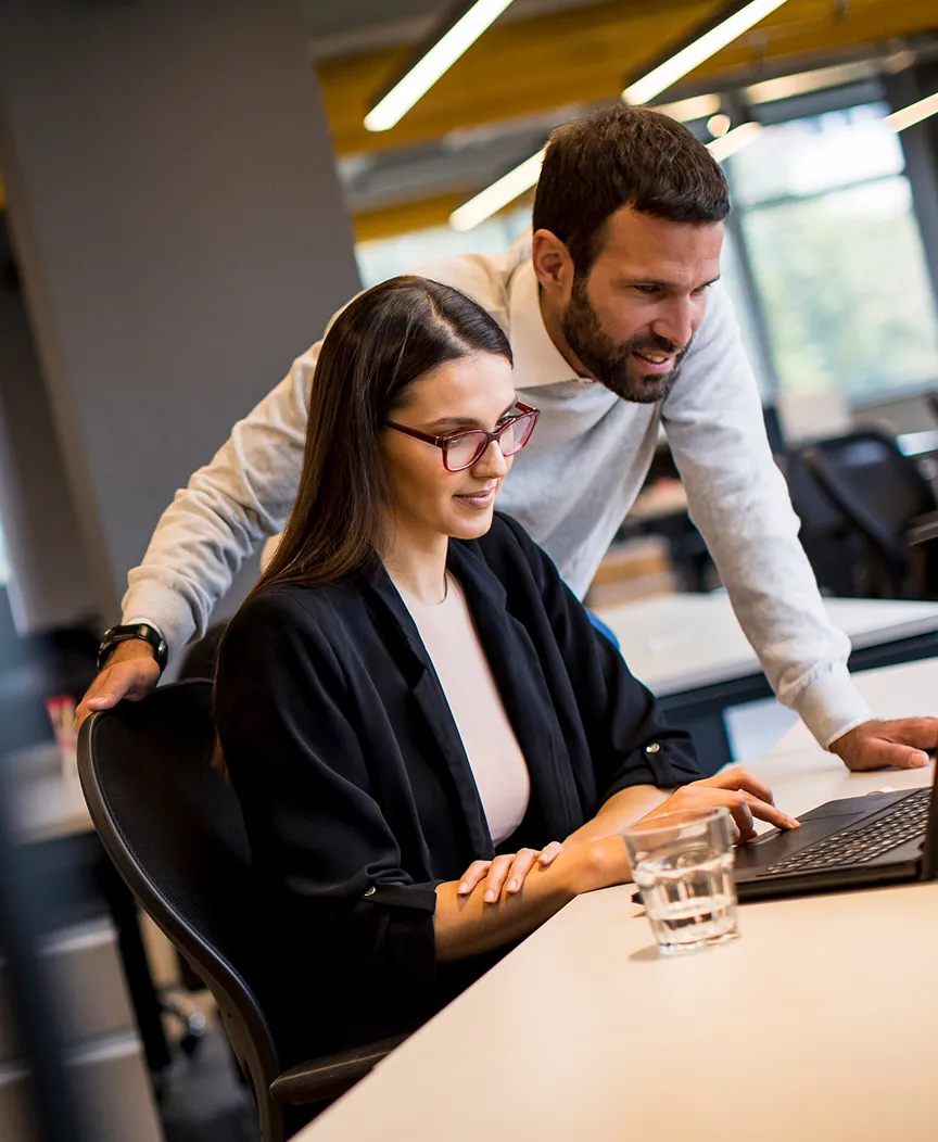 A man and woman in an office looking at a laptop