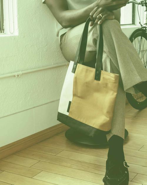 Image of a black man from the chest down sitting holding a phone and bag