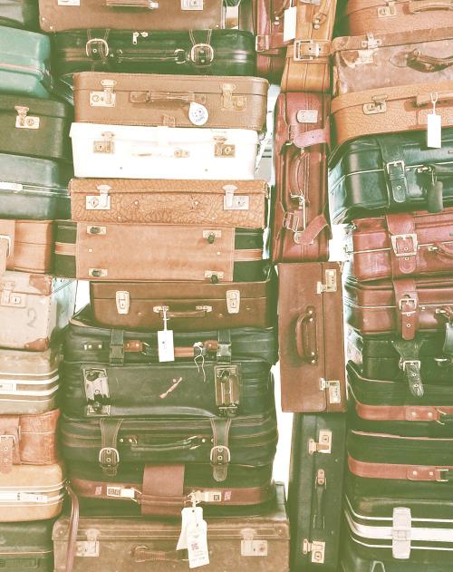 Dozens of vintage suitcases are stacked on top of each other and side by side