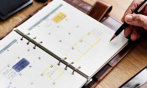 A calendar planner open with someone writing in it with a pen